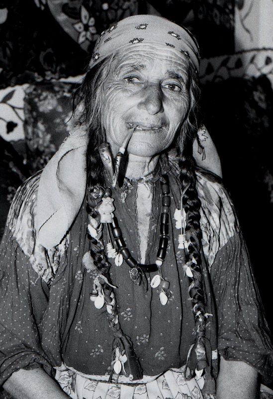jakabtibor - Old gypsy woman. 85 years old gypsy woman smoking her pipe. shes wearing traditional dress, having shells in her hair.. Zdjęcie 48982